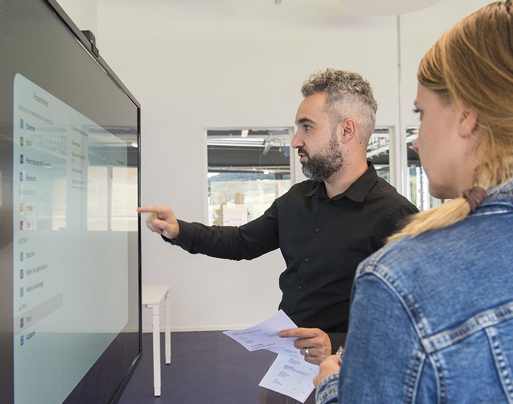 photo de profil d'une femme et un homme devant un grand écran interactifs