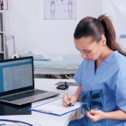 medecin entrain de prendre des notes sur une table dans un cabinet medical avec un ordinateur
