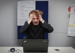 homme se tenant les cheveux avec un tête désespérée assis face à un ordinateur dans une salle de conférence