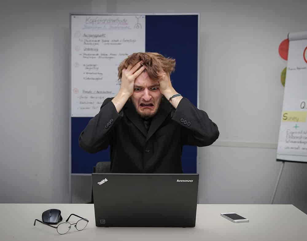 homme se tenant les cheveux avec un tête désespérée assis face à un ordinateur dans une salle de conférence